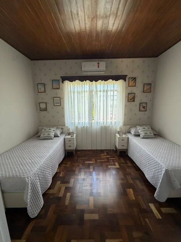Quarto com duas camas arrumadas, criados-mudos, ar-condicionado e forro de madeira.