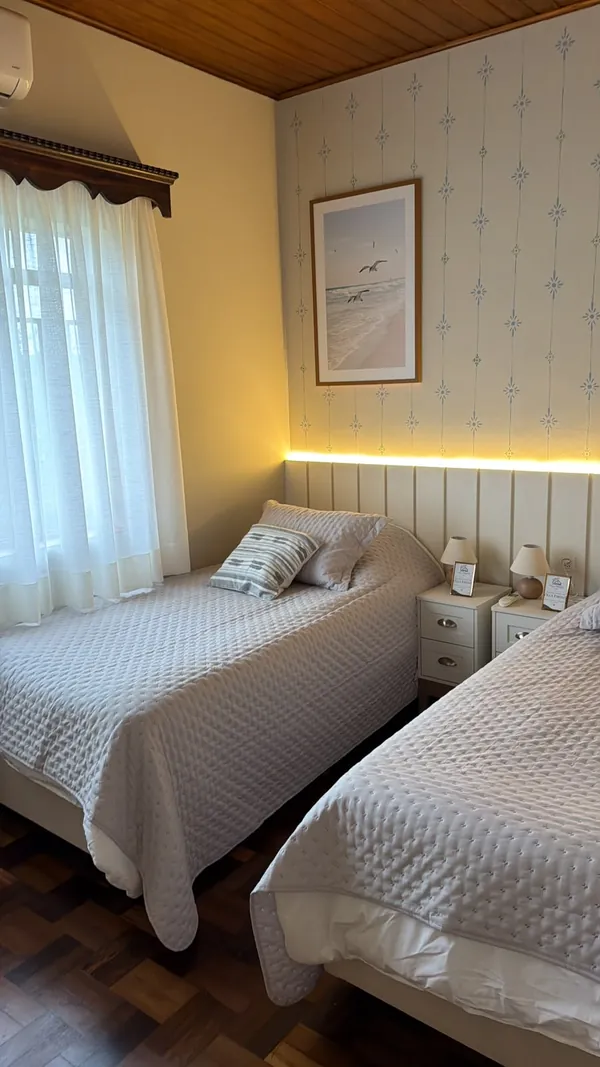 Quarto com cabeceira de móveis planejados, luz suave e quadro de paisagem marinha.
