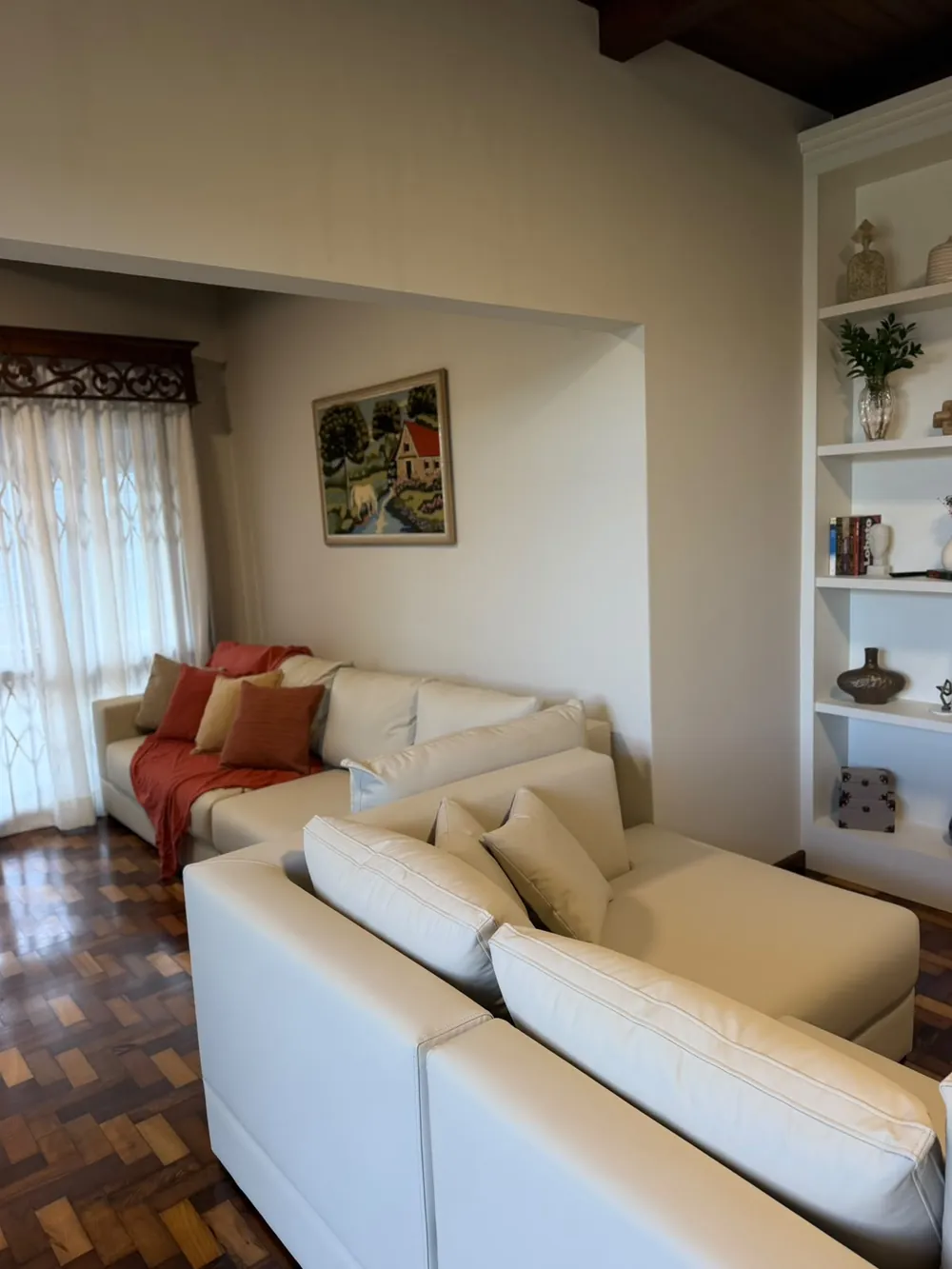 Sala de estar do Villa Firenze, com sofá branco, almofadas terrosas e estante planejada, onde a família é recebida.